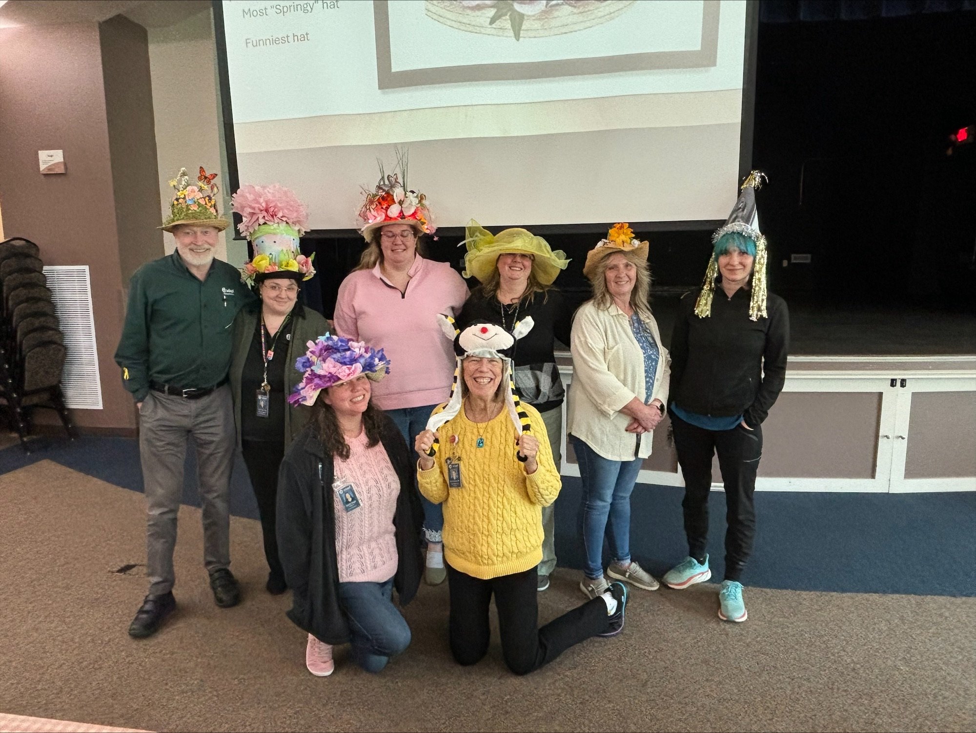 Primary Care Hat Day: A group of Adapt Integrated Health Care employees wearing creative and colorful hats, posing for a fun group photo indoors.