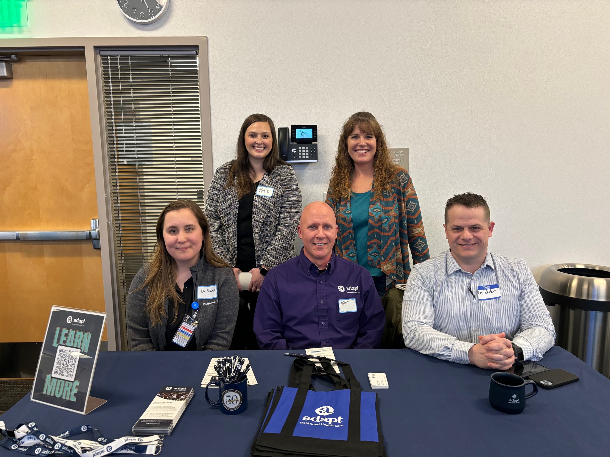 Provider Hiring Summit: Five Adapt Integrated Health Care employees sit behind a table at a hiring summit, with informational materials and promotional items displayed.