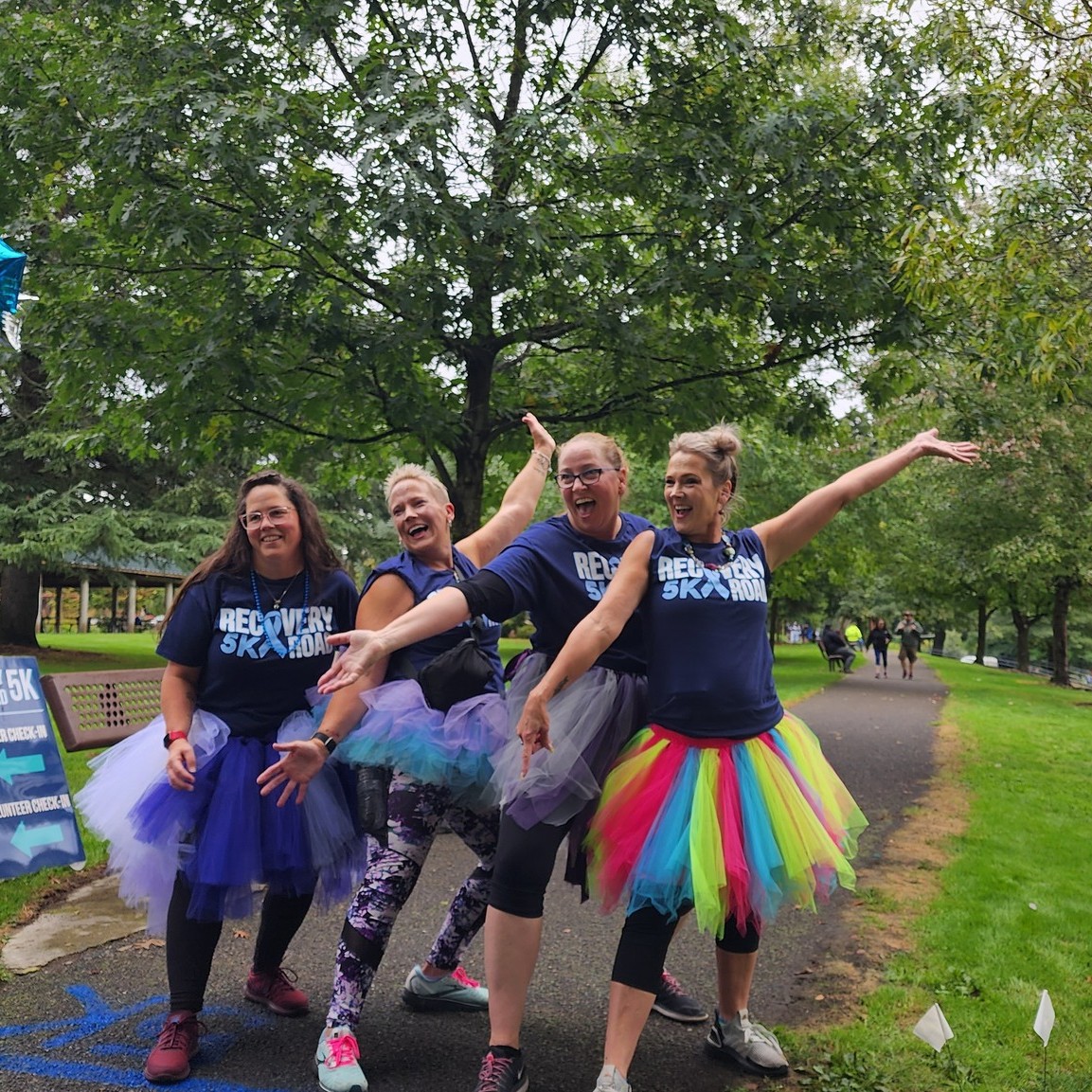 Recovery Road 5K 2024: Four Adapt Integrated Health Care employees dressed in colorful tutus and matching T-shirts, posing joyfully during the Recovery Road 5K event.